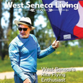 Man in blue shirt and hat flying a large kite outdoors, with “West Seneca Living” magazine text.