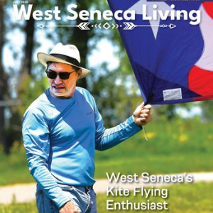Man in blue shirt and hat flying a large kite outdoors, with “West Seneca Living” magazine text.