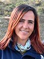 Una mujer con cabello largo y rojo y una bufanda alrededor del cuello sonríe para la cámara.