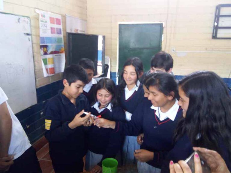 Un grupo de niños mira un teléfono celular en un aula.
