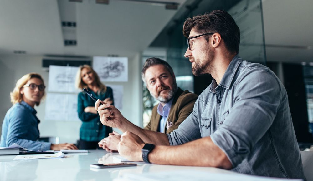 A group of people are sitting around a table having a meeting discussing IT hardware.