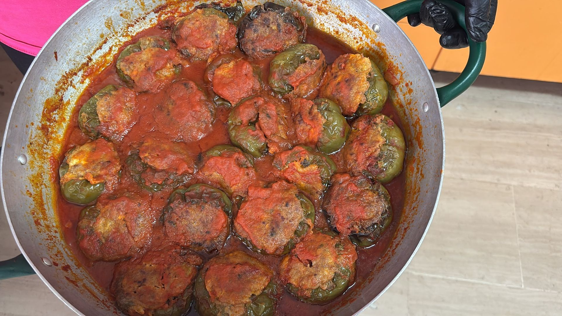 Vista dall'alto di una padella piena di salsa di pomodoro rosso e peperoni ripieni o fette di zucchine rosolate che cuociono sul fornello.