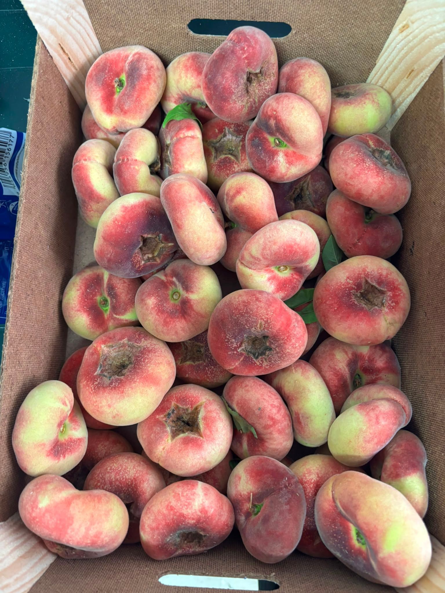 Scatola piena di pesche mature, alcune con sfumature rosse e buccia vellutata.