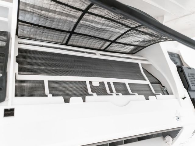 A white split-system air conditioner unit with its front panel open, revealing the internal dust filter and cooling coils.