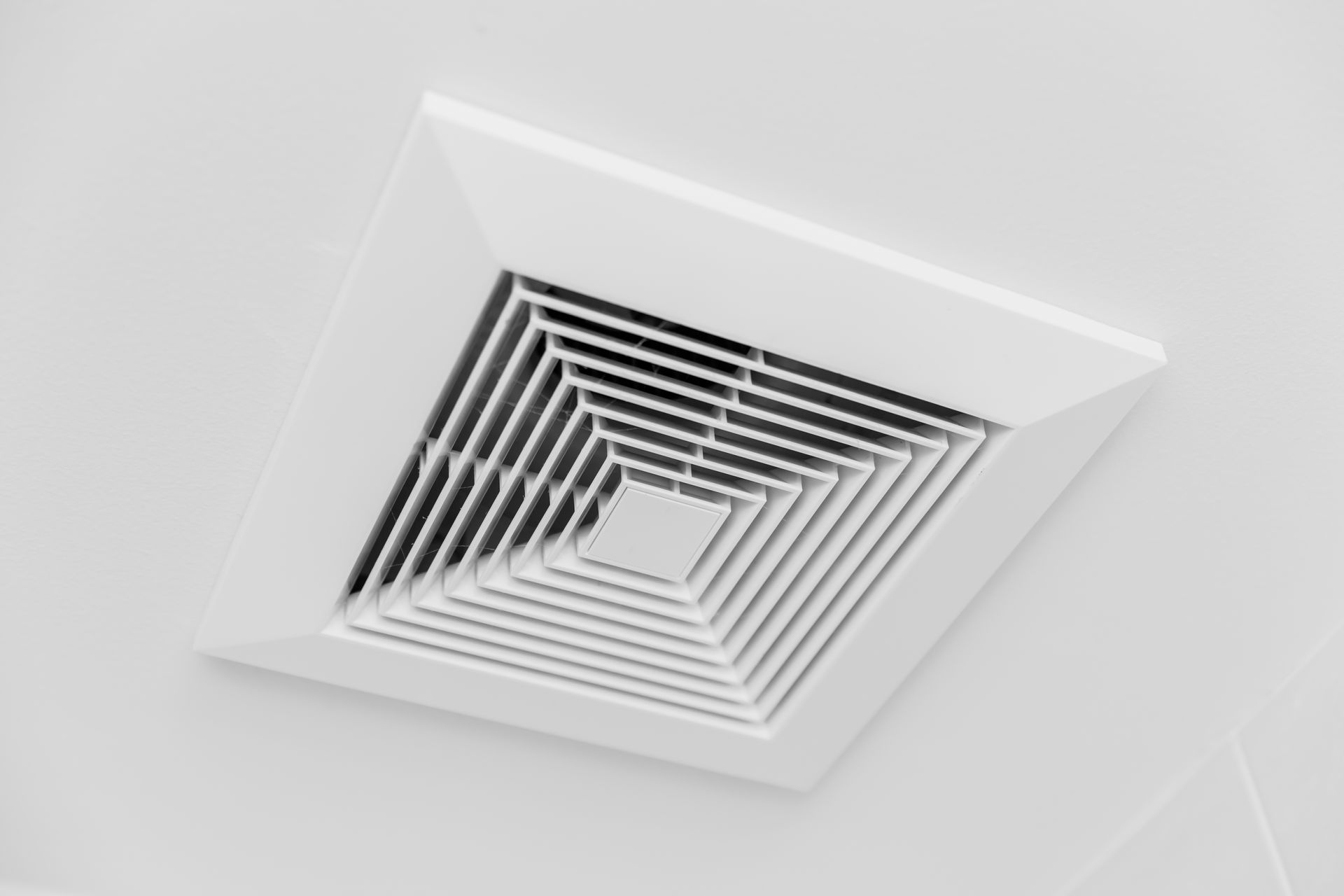 A square white ceiling air vent with concentric louvered slats mounted on a plain white ceiling.