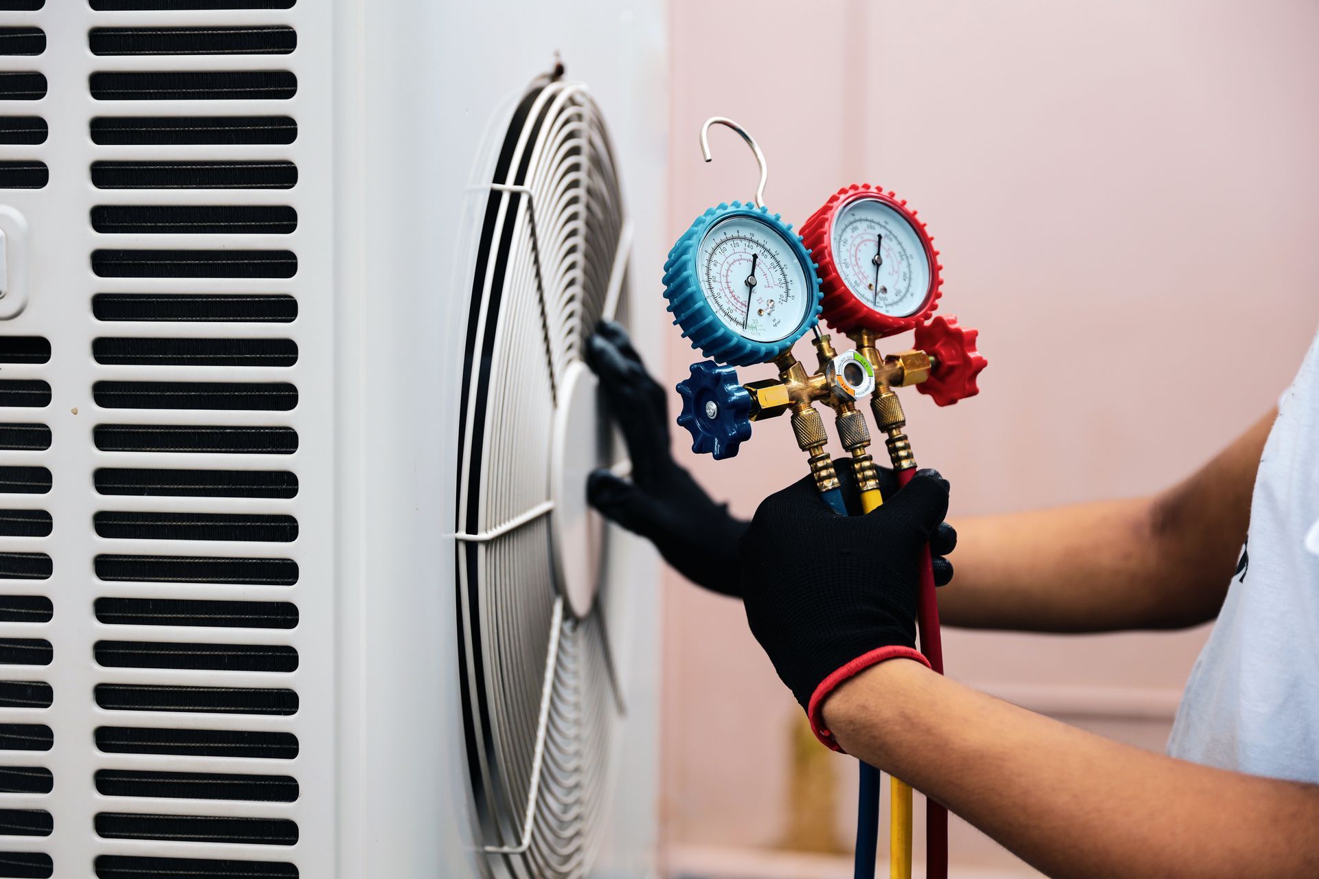 A technician in black gloves uses a manifold gauge set to service an air conditioning unit.