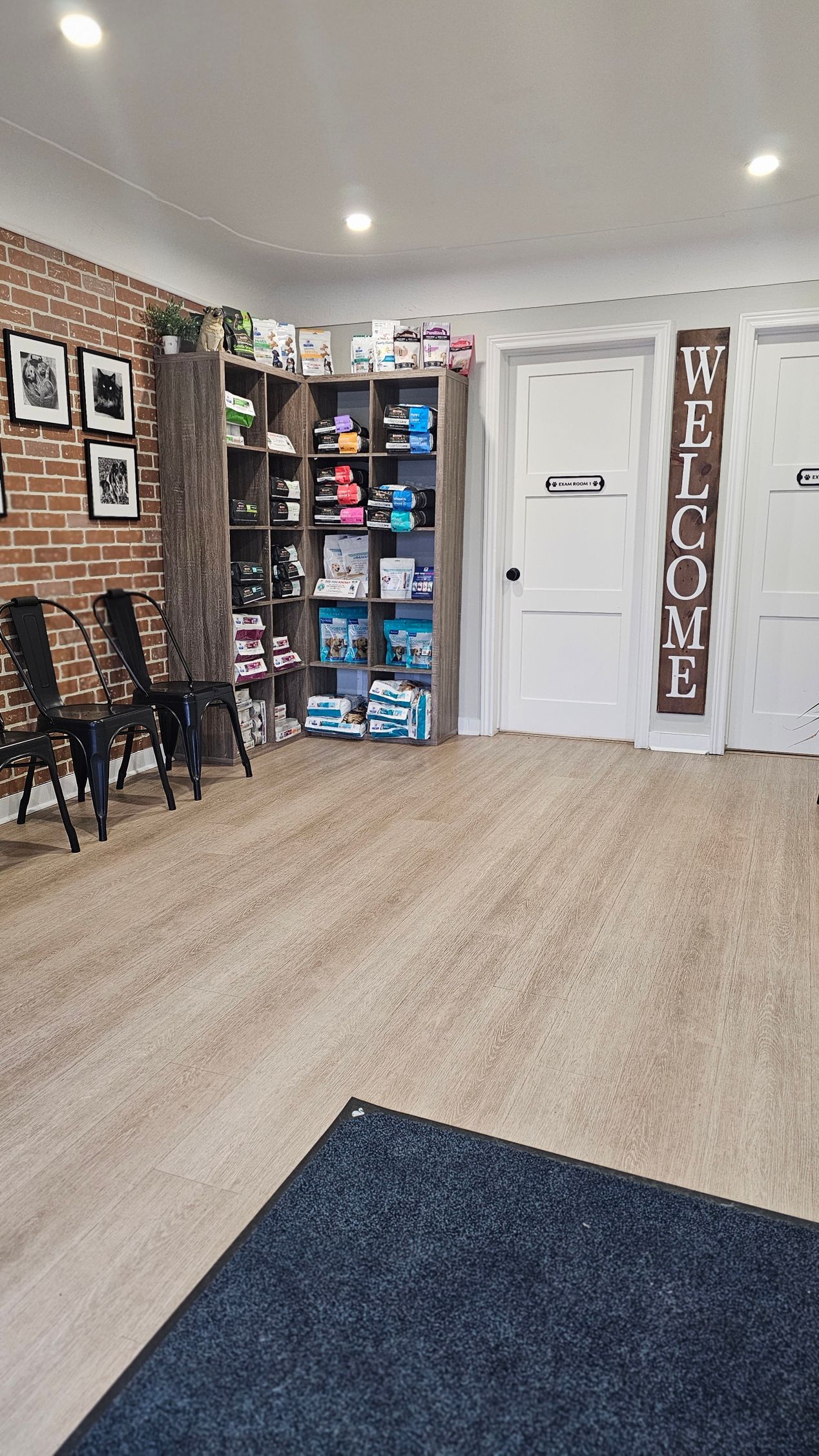 Waiting room with brick wall, chairs, shelves of products, white doors, and rug.