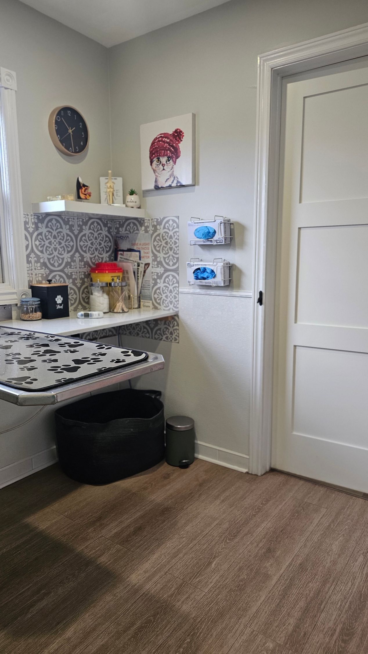 Corner room with a desk, shelf, and storage. Black pet bed, trash can, and door visible.