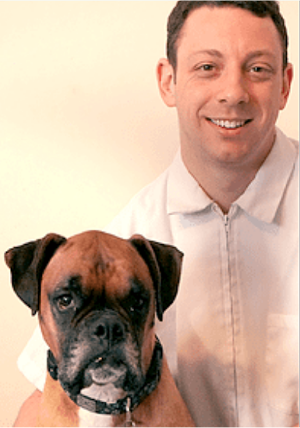 Man with dog, both looking forward. Man wears white coat, smiles. Boxer dog wears collar, has brown and white fur.