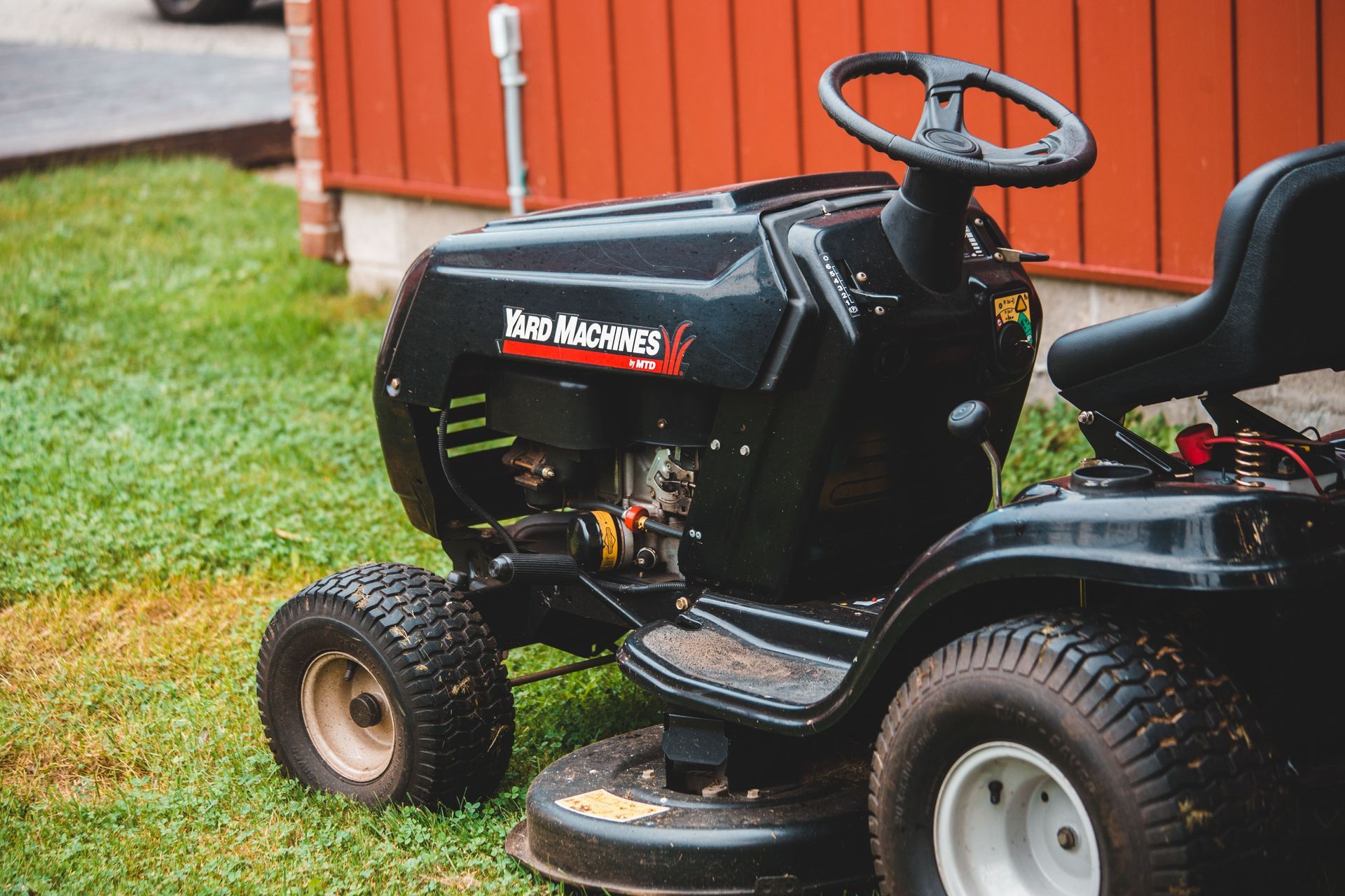 Green lawn mower on a manicured suburban lawn with flower beds and trees in the background
