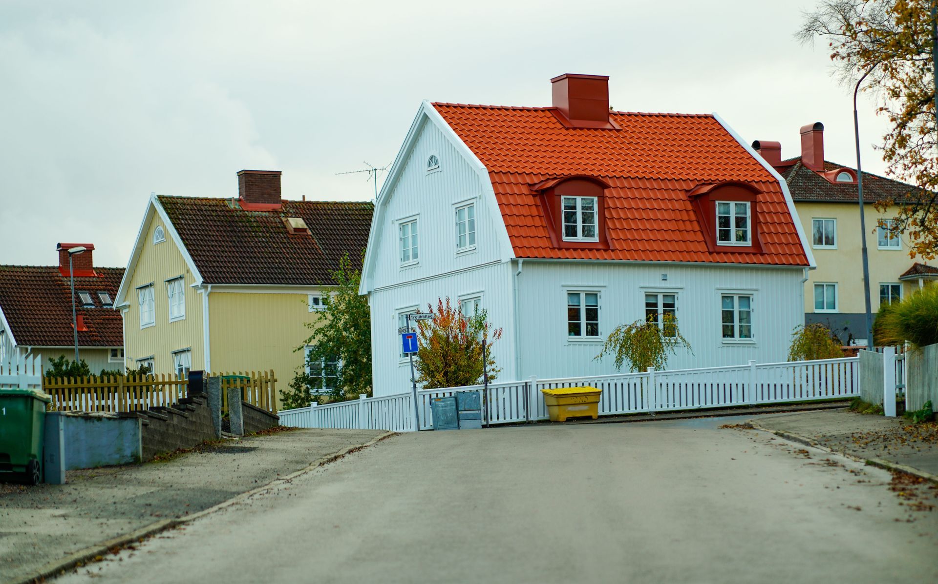 Quiet residential street with white and yellow houses, red roofs, and a large paved road bend