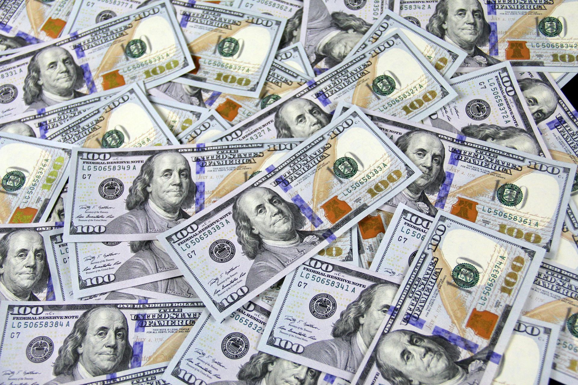 Pile of $100 bills, Benjamin Franklin's portrait visible, with a green and tan color scheme.