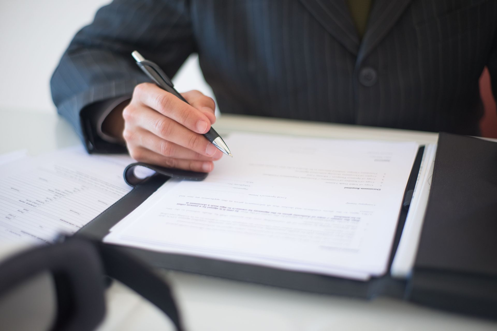 Hand signing a document on a clipboard at a desk