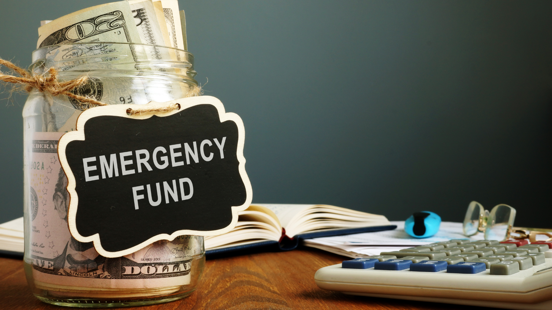 Emergency fund jar with cash on a desk beside calculator and notebook
