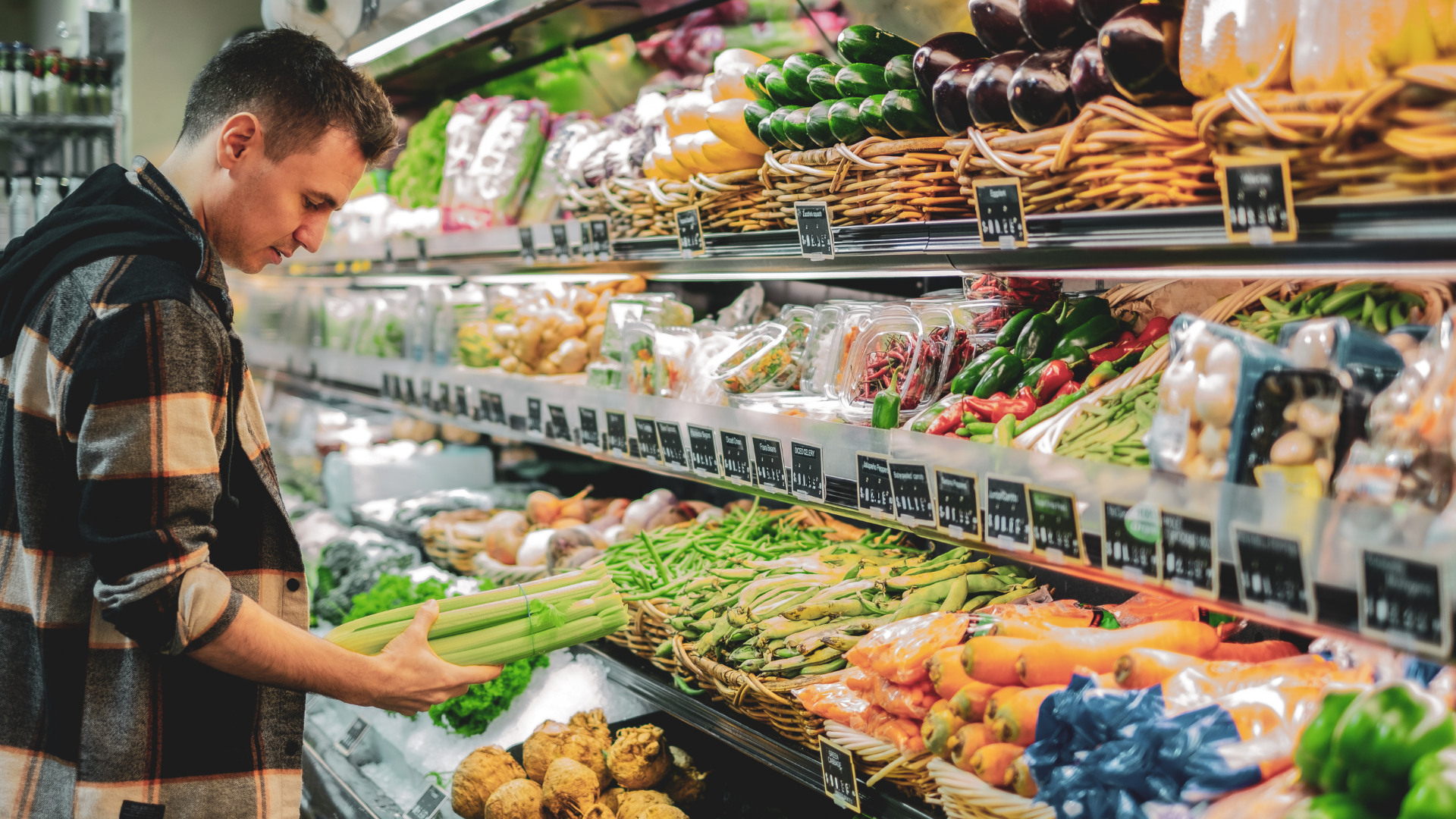 Shopper selecting fresh produce in a supermarket aisle with colorful fruits and vegetables.