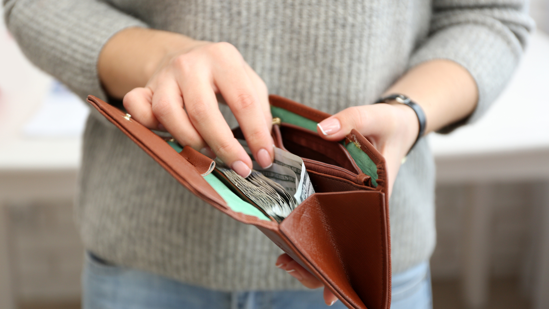 Person holding open brown wallet and counting cash inside.