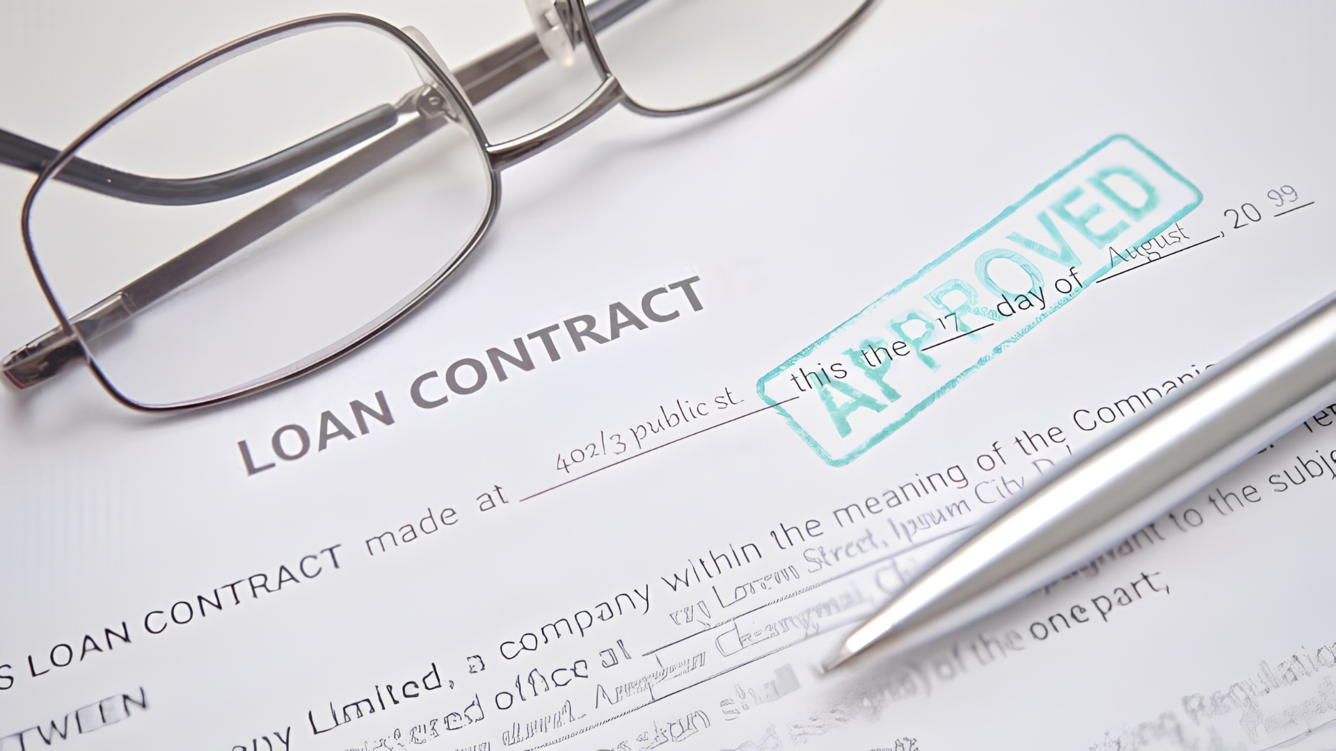Loan contract with glasses and pen, stamped “APPROVED” in teal on the document.