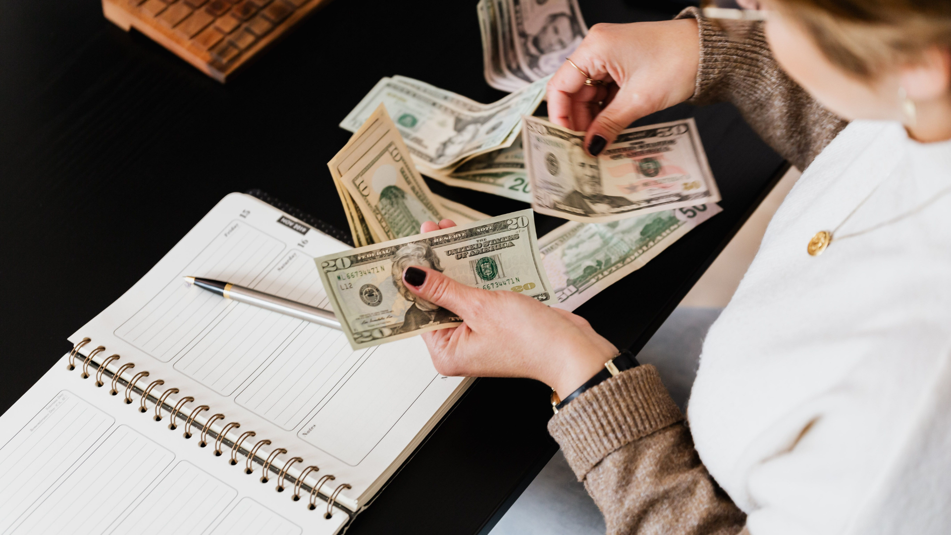 Hands counting cash beside a budget and pen on a desk