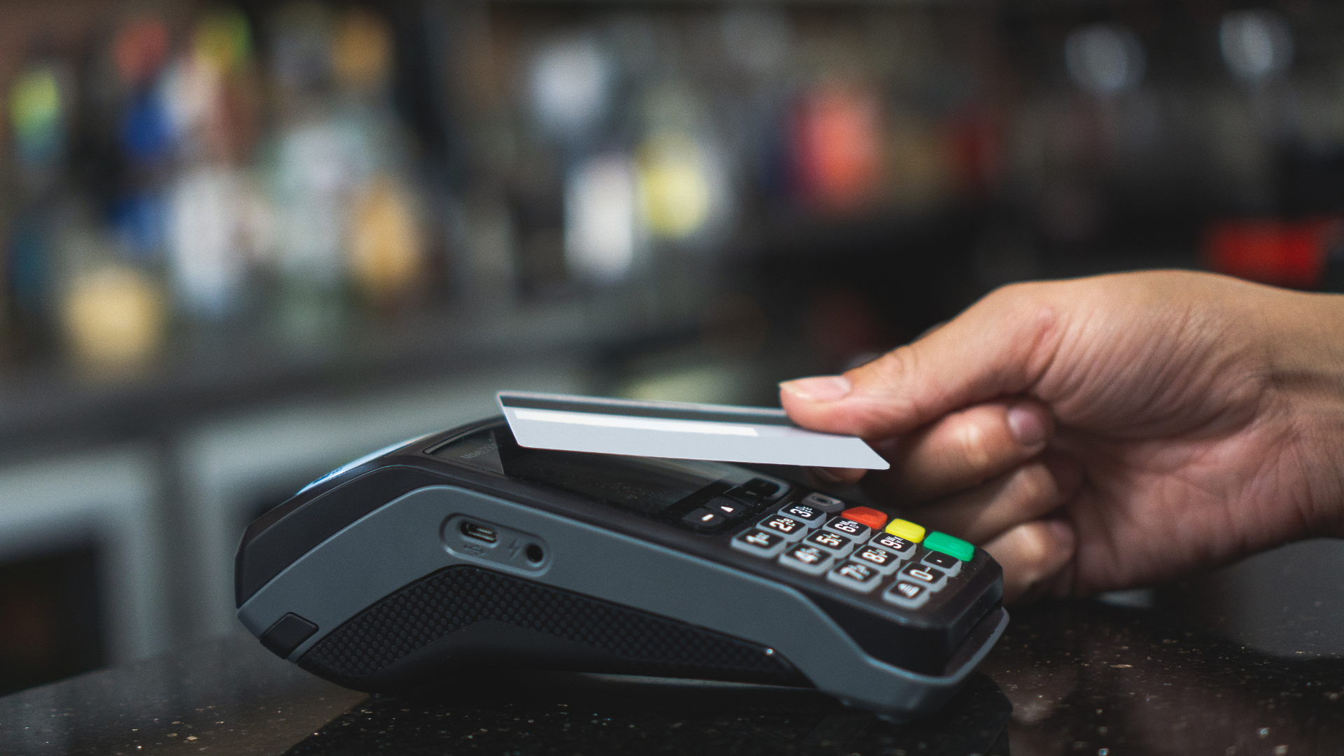 Hand tapping a credit card on a payment terminal at a checkout counter