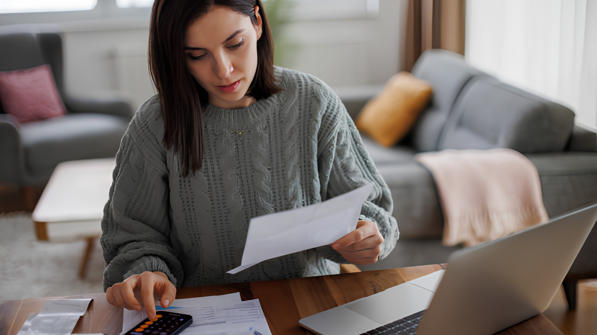 Person reviewing papers at a laptop on a sofa in a living room