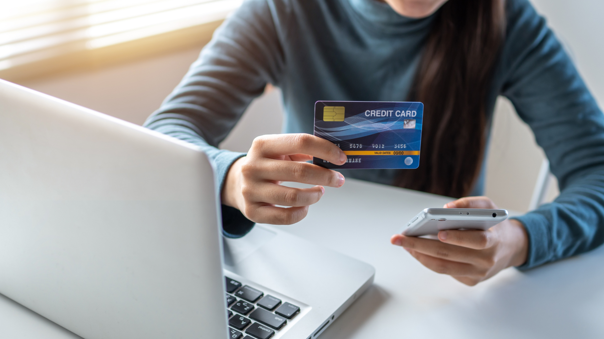 Person using laptop while holding a credit card and smartphone for online shopping