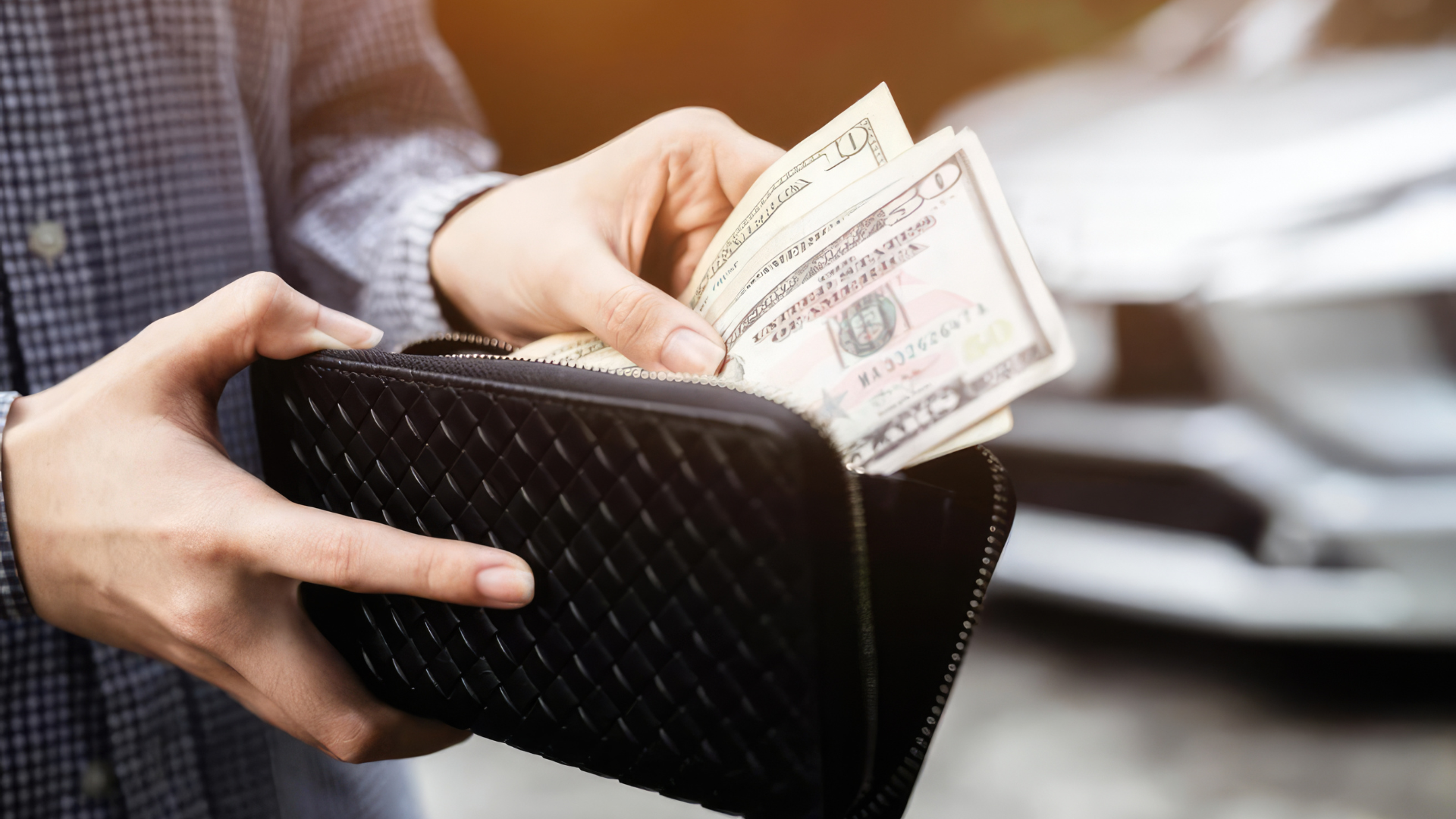 Hands pulling cash from a black quilted wallet in a blurred indoor setting