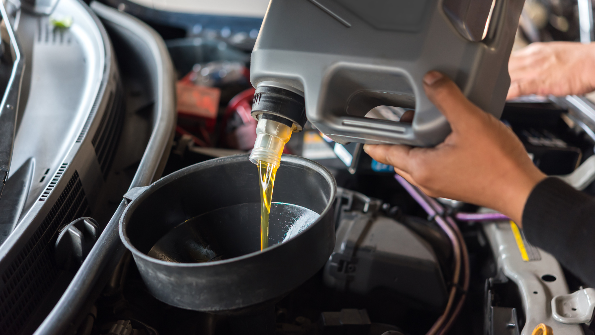 Motor oil pouring from a gray container into a black pan in an engine bay
