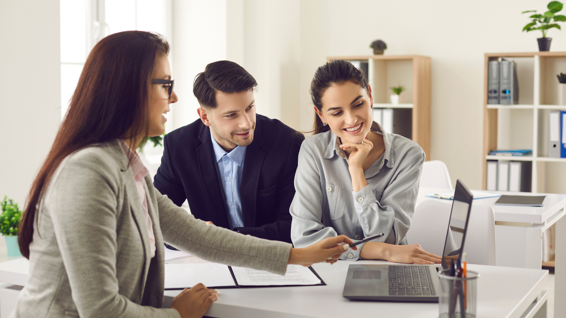 Three coworkers reviewing documents and a laptop in a bright office meeting area