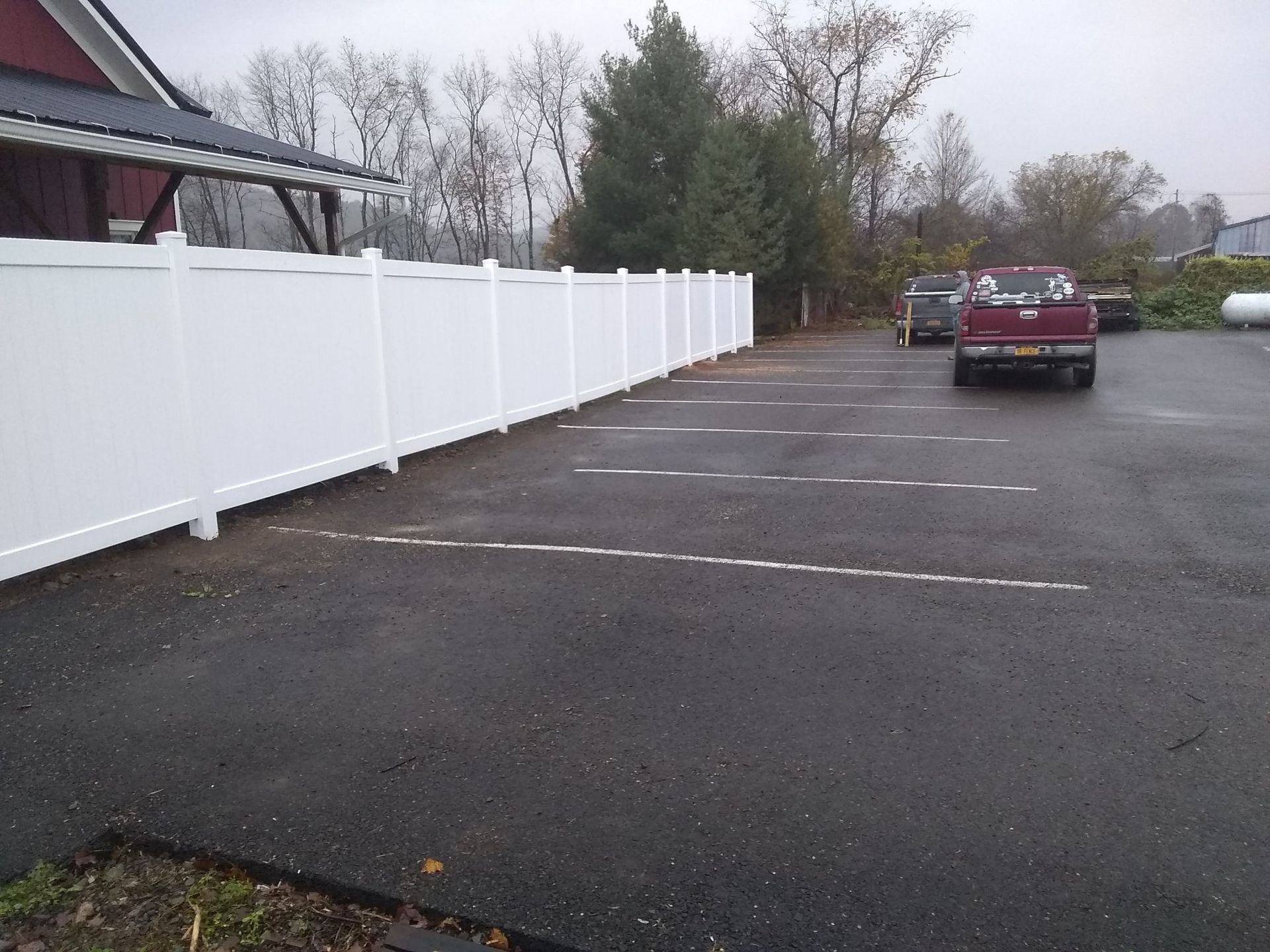A red truck is parked in a parking lot next to a white fence