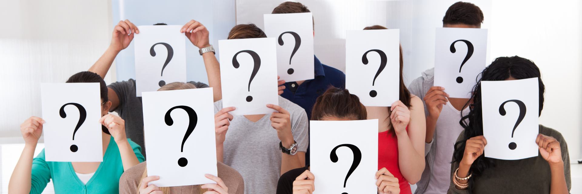 People holding white signs with black question marks, covering their faces in a group photo.