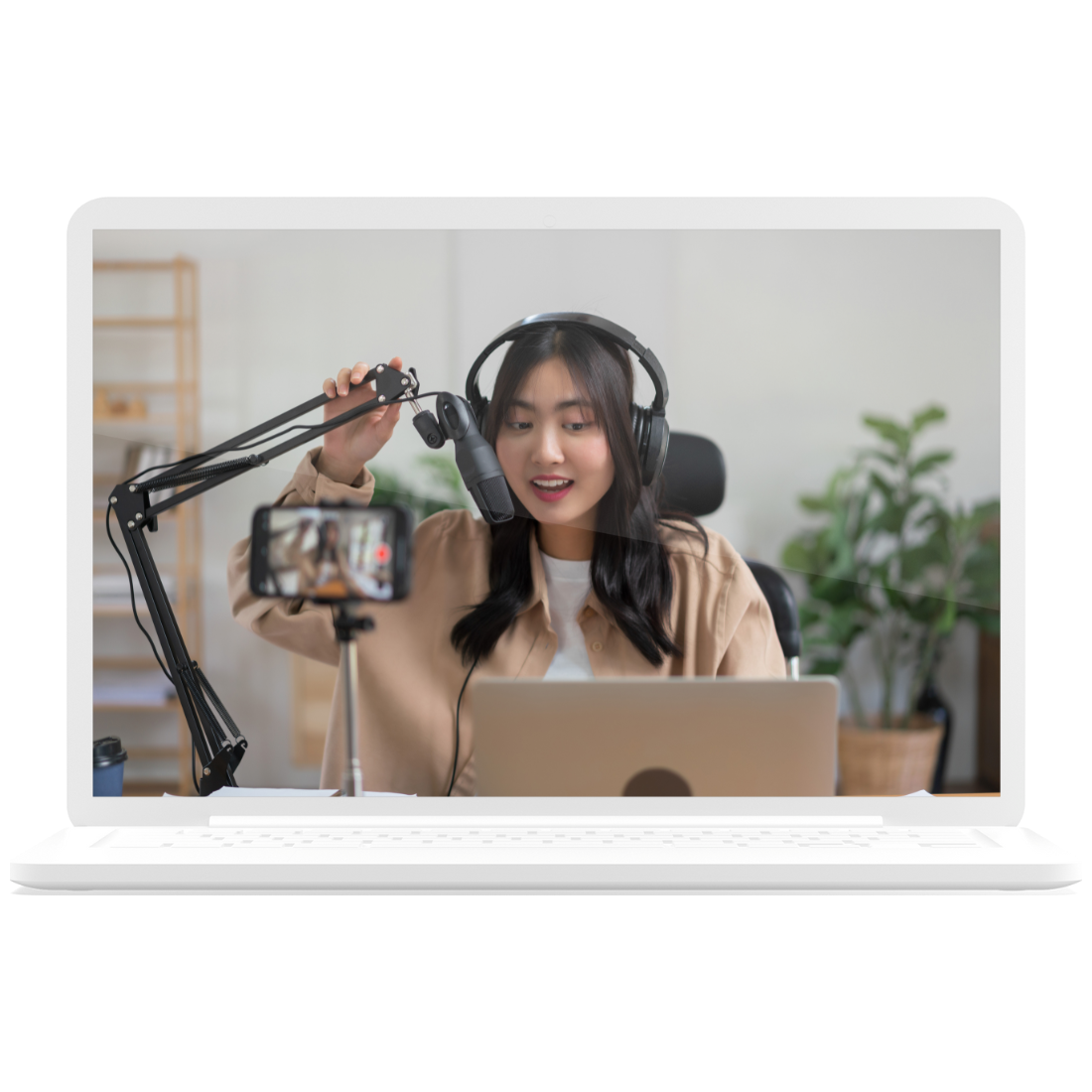 Woman recording a podcast at a desk, speaking into a microphone beside a laptop and phone camera