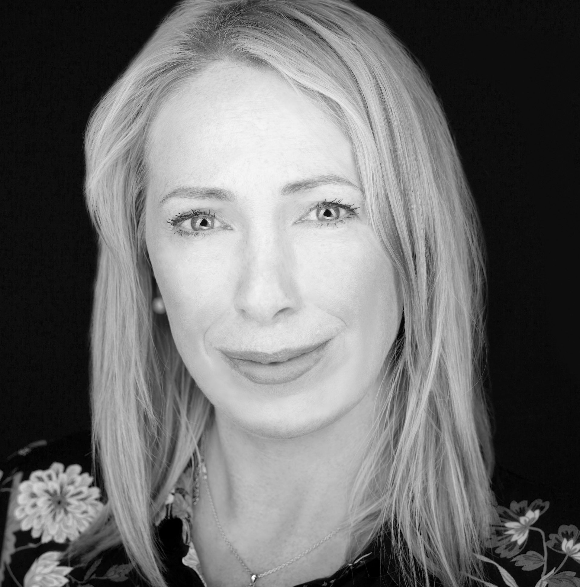 Woman with blonde hair smiles, wearing a floral top.