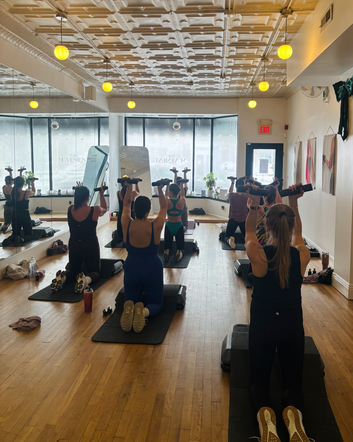 a strength training class lifts weights in a sunlit studio