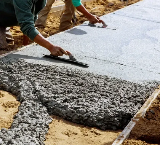 A man is spreading concrete on a sidewalk with a trowel