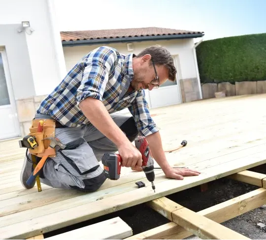 A man is working on a wooden deck with a drill