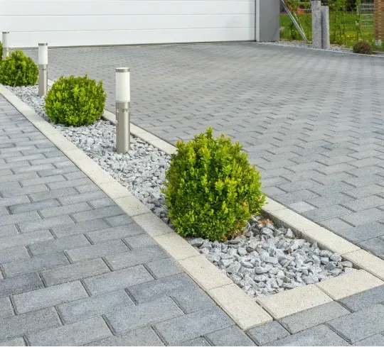 A brick driveway with plants and rocks in the middle