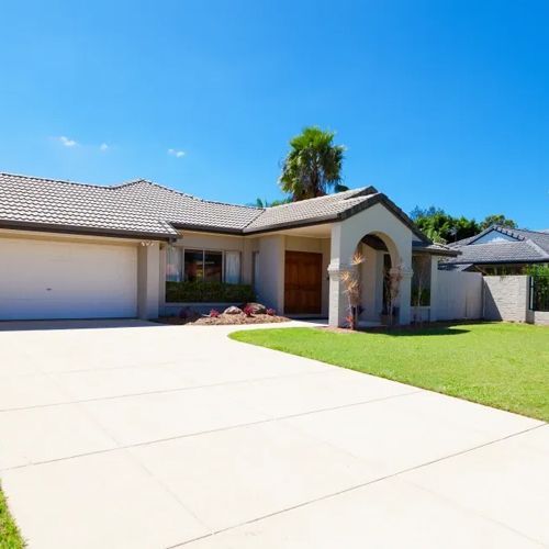 A white house with a large driveway and a palm tree in the background