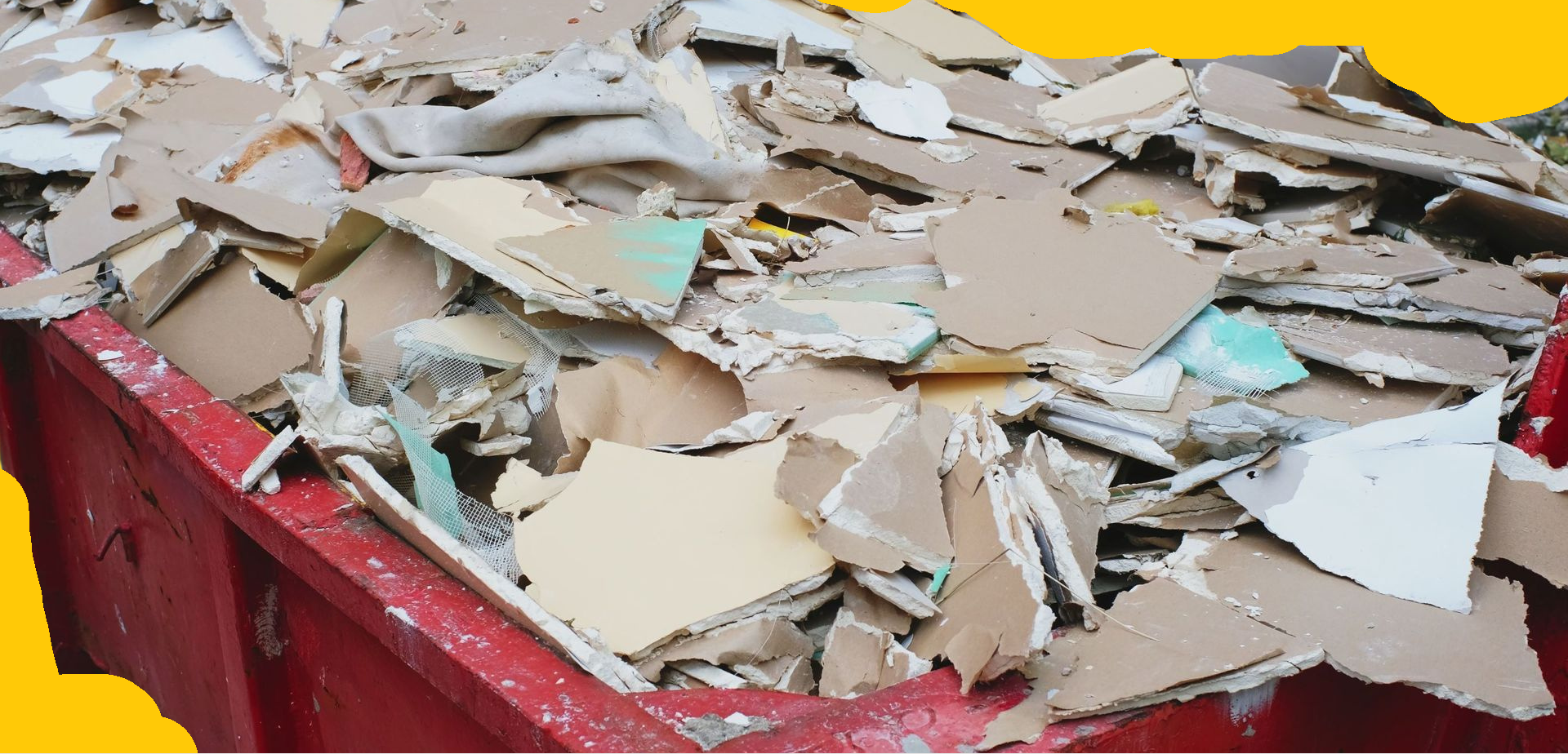 Pile of construction debris in a red dumpster. The debris consists of broken pieces of drywall, plaster, and other construction materials.