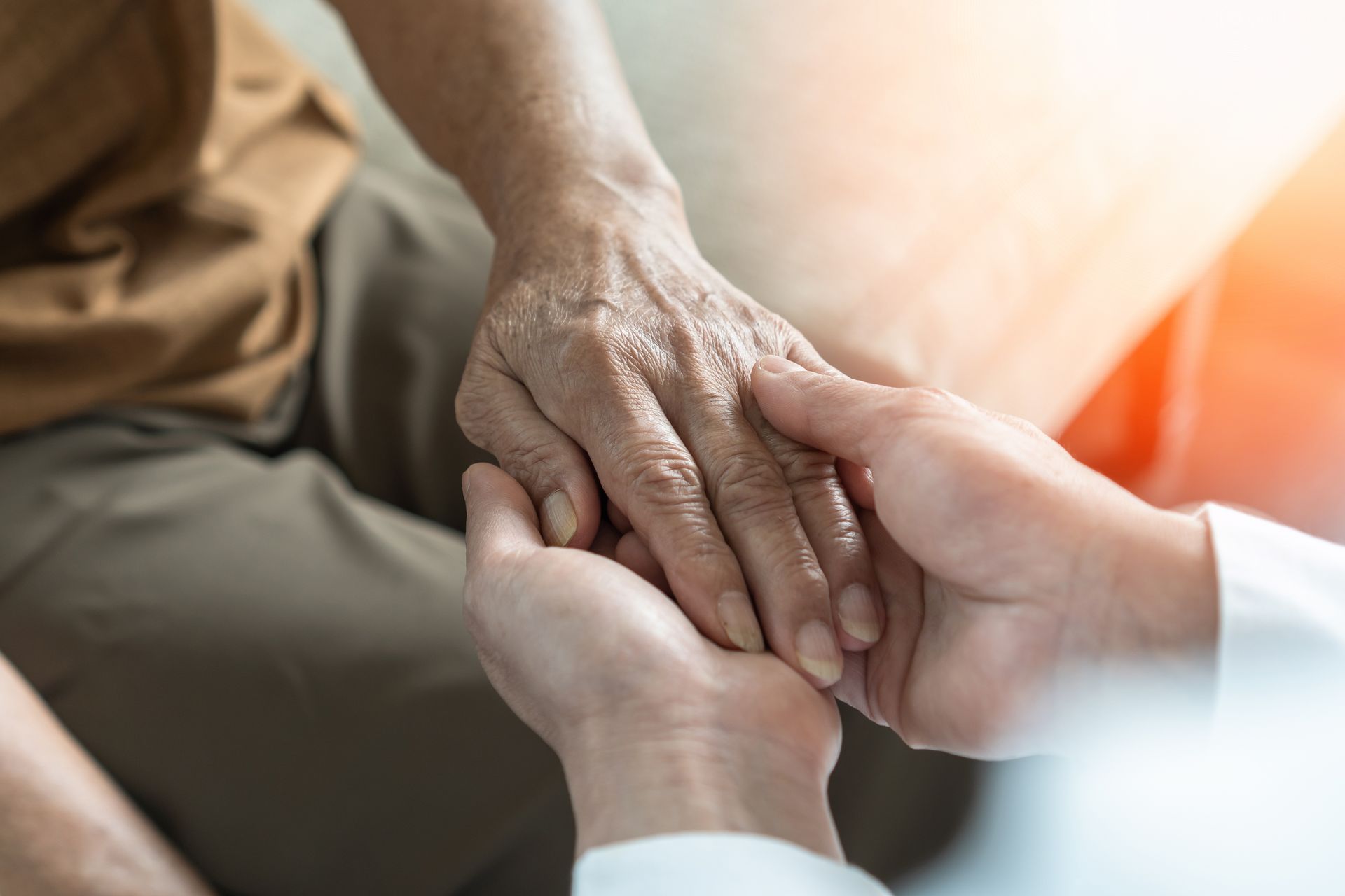 A person's hand held by another person's hand; offering comfort and care, lit by sunlight.