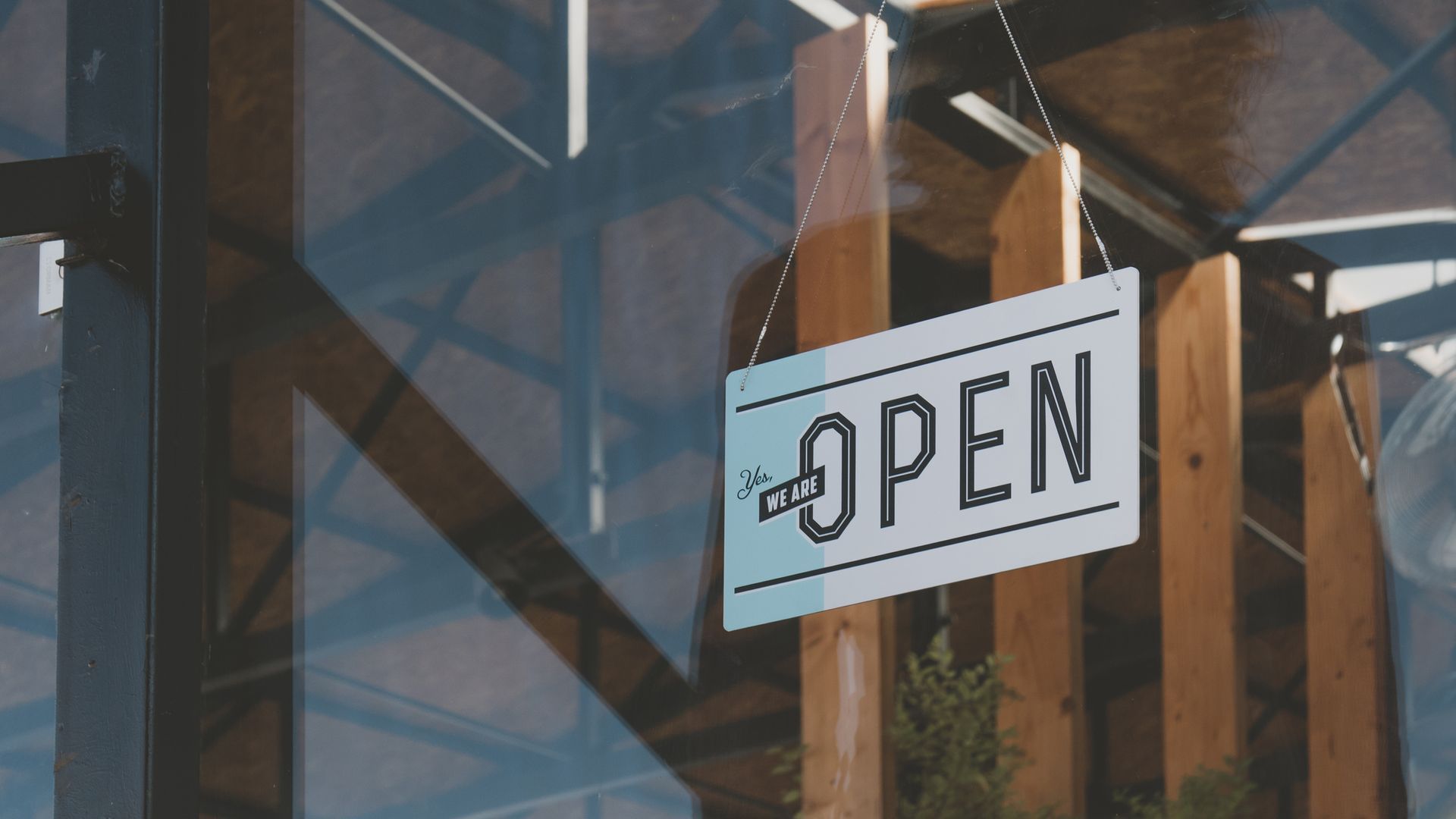 Open sign hanging on a wooden post in front of a glass window.