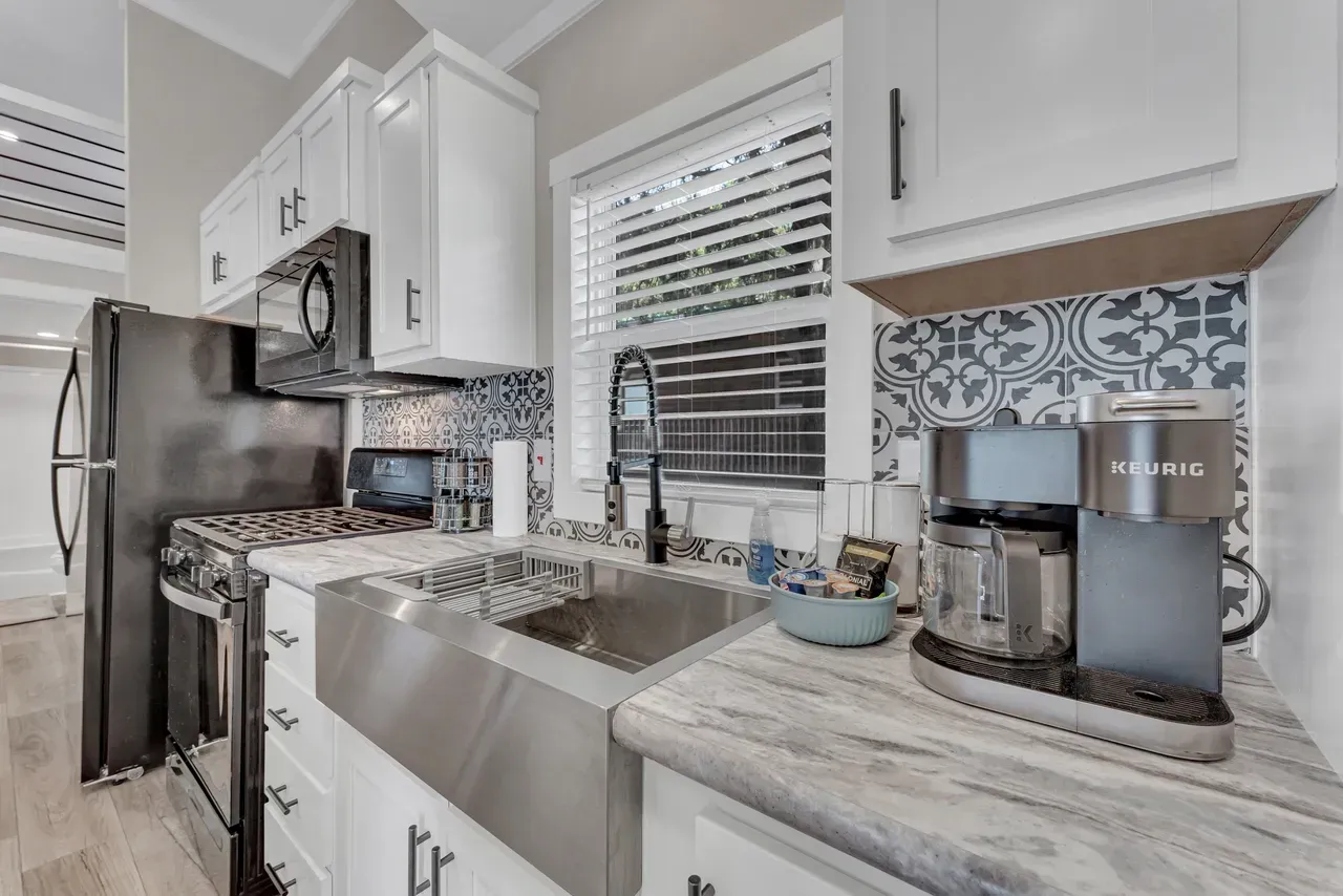 Kitchen with white cabinets, stainless steel sink, coffee maker, and blue patterned backsplash.