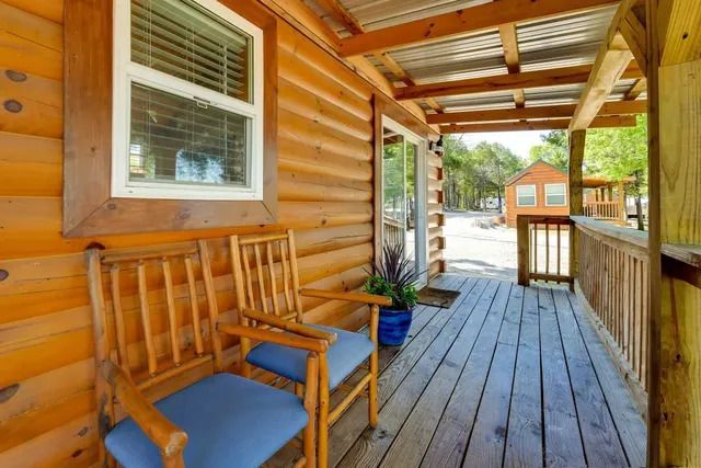 Wooden cabin porch with two chairs, window, and a small flower pot.
