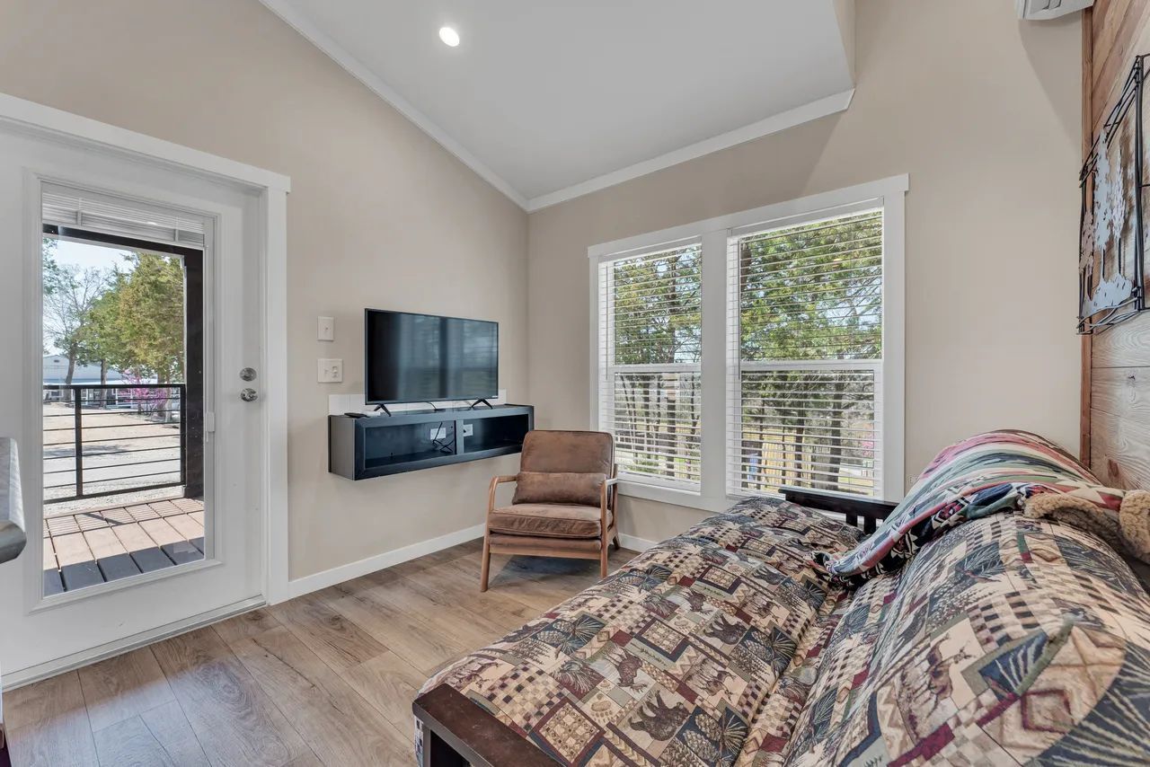 Living room with a sofa, TV, chair, and a door opening onto a deck with a view.