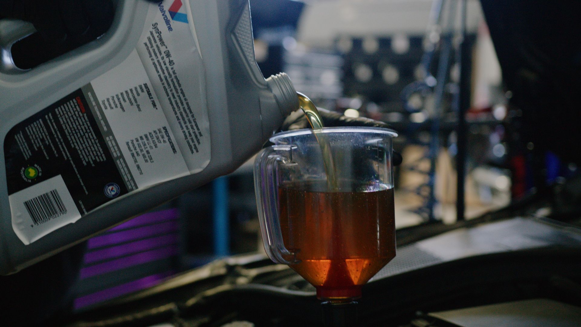 Gray container pouring amber liquid into a clear plastic cup in a dim workshop setting