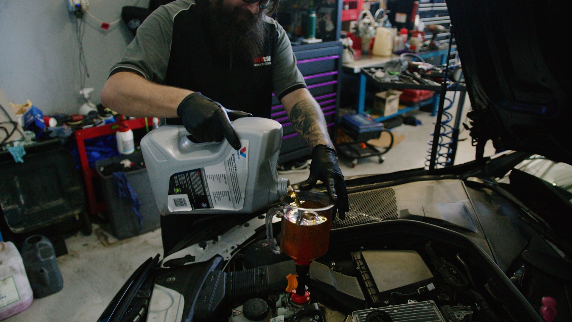 A mechanic in a garage reviews digital diagnostics on a tablet while inspecting an open car engine.