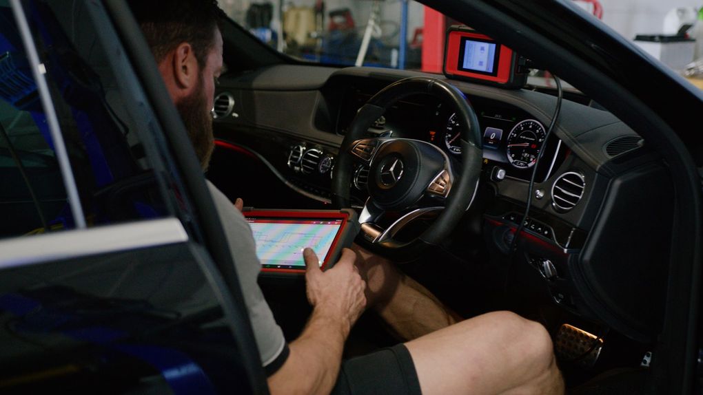 Man sitting in a car at night, using a tablet while the dashboard and steering wheel are visible
