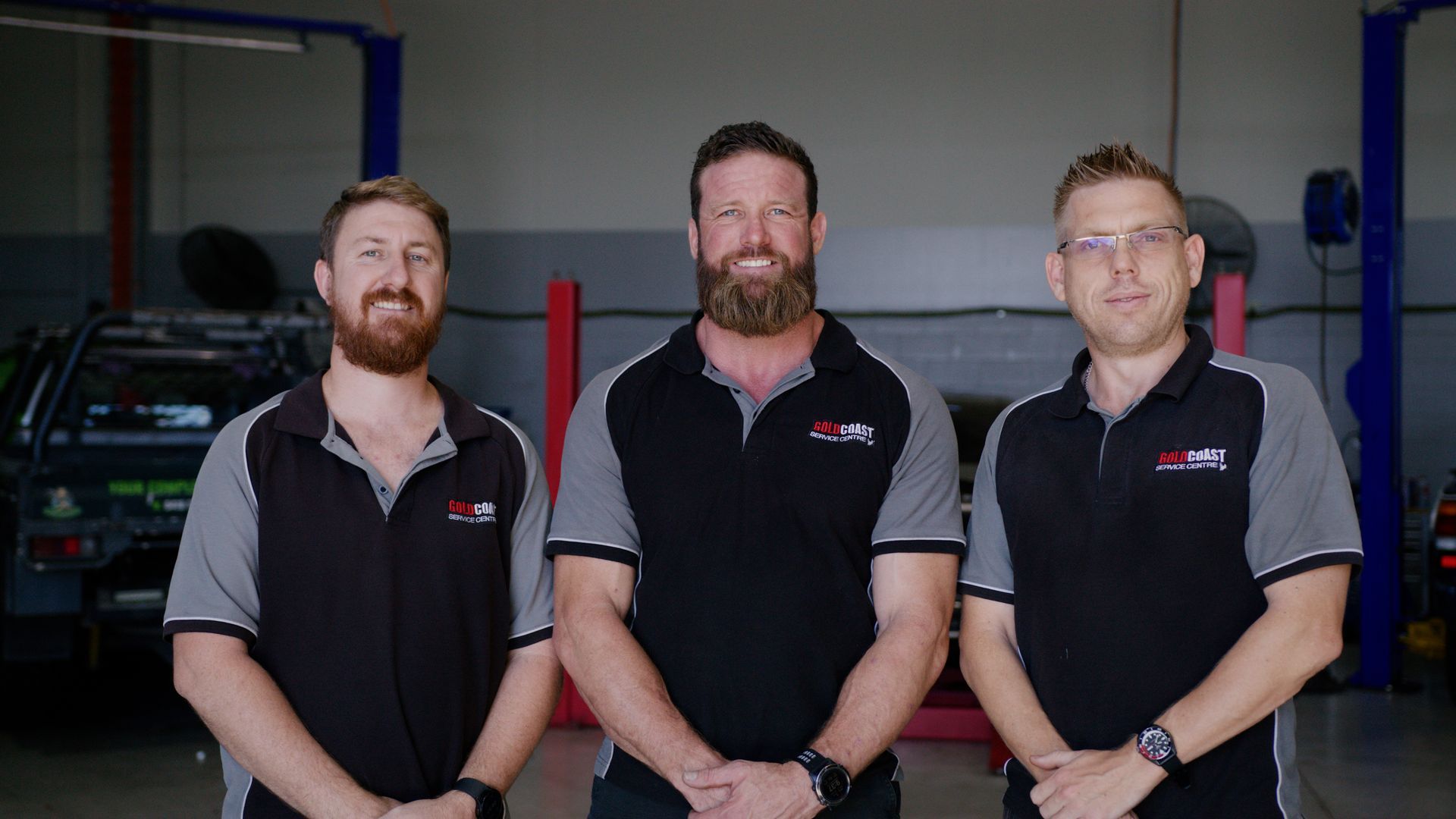 Three mechanics in black and gray uniforms standing in a garage