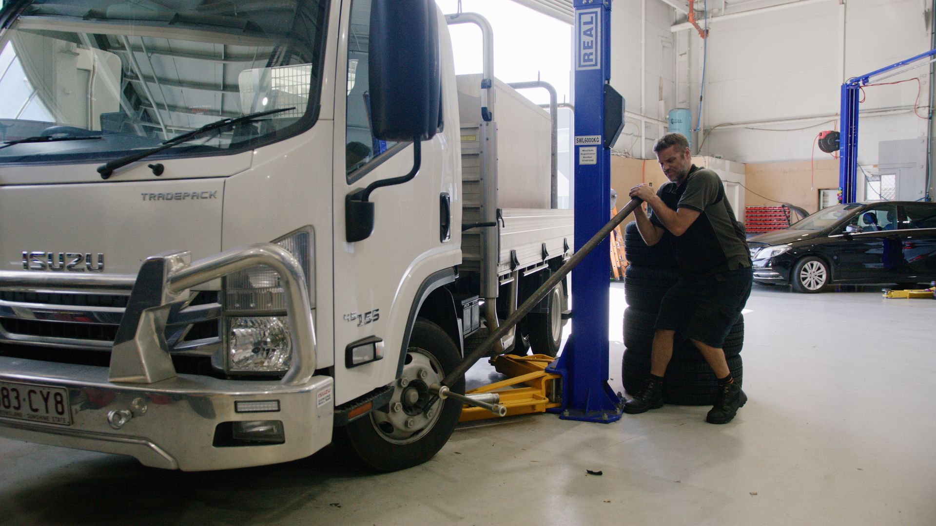 Mechanic inspecting a white truck on a lift inside an auto repair shop
