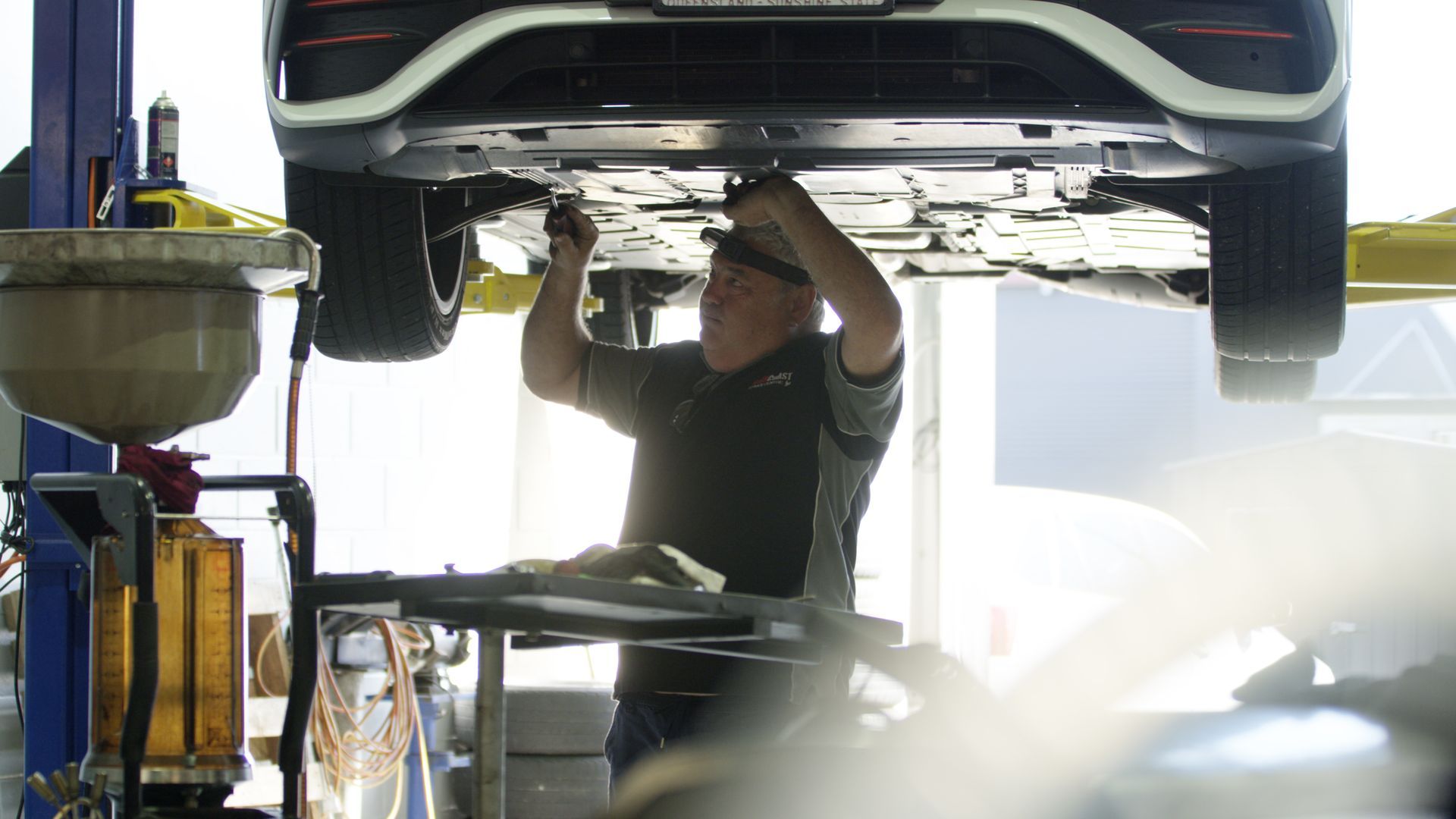 Mechanic working under a raised car in an auto repair shop, with tools and equipment nearby