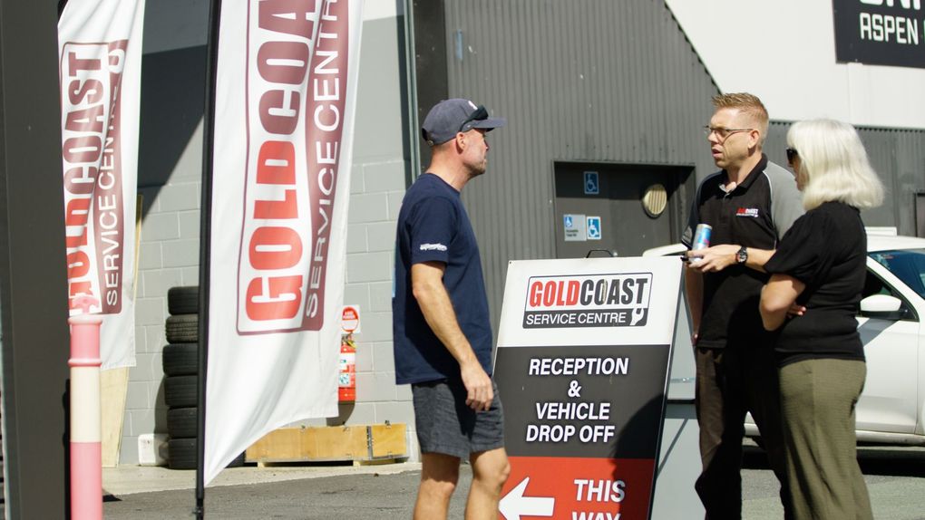 Three people talking outside a Goldcoast building beside a sale sign.